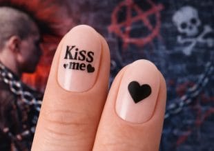 Nærbilde av to fingre med neglelakk; på den ene neglen står det Kiss me with hearts, på den andre er det et svart hjerte. I den uskarpe bakgrunnen ser vi en person med mohawk og vegggraffiti med en hodeskalle og et anarkisymbol.