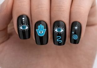 A hand with black nail varnish featuring blue and white mystical designs, including an eye, a hamsa hand, spirals, stars, and dots on each fingernail.