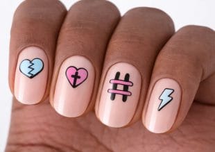 En hånd med fire fingernegler, hver dekorert med forskjellig pastellfarget neglekunst: et blått knust hjerte, et rosa hjerte med et svart kors, to rosa streker med en svart hashtag og et hvitt lynnedslag.